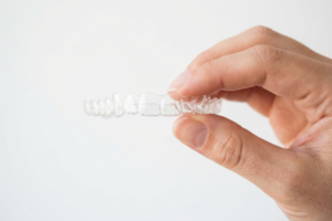 Person holding a clear Invisalign aligner tray between their fingers